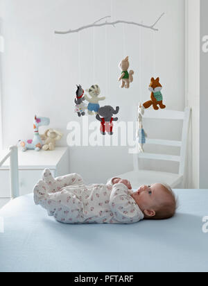 Baby girl giacente sul retro che si affaccia fino al mobile animale, 3 mesi Foto Stock