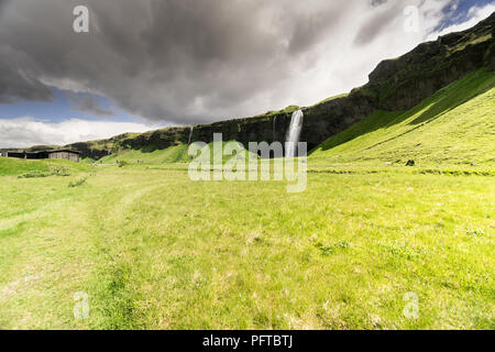 Irriconoscibile turisti occupano il sentiero towrads la cascata Seljalandsfoss, una delle fermate di Islanda del popolare percorso turistico. Foto Stock