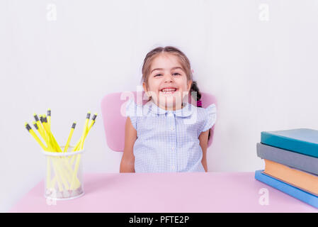 Carino poco felice ragazza in uniforme scolastica si siede e ridere.messa a fuoco selettiva e spazio di copia per la modifica Foto Stock