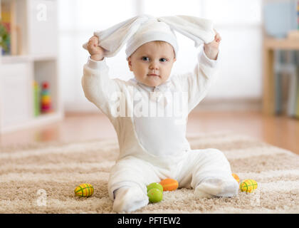 Funny Baby girl in costume di coniglio sitying sul tappeto nel vivaio Foto Stock