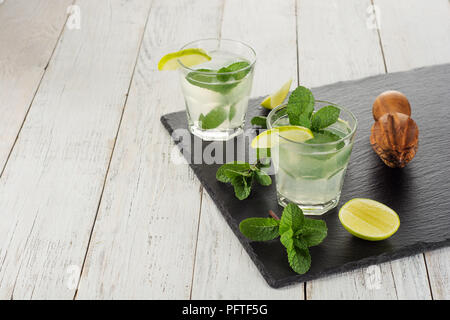 Bevanda estiva. Citrus limonata con la menta e il ghiaccio sul bianco sullo sfondo di legno. Foto Stock