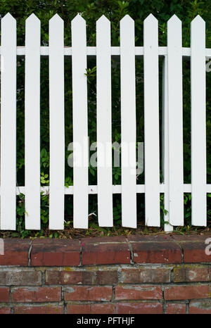 Fence Picket in legno Dipinto di bianco su una base di Mattoni rossi Foto Stock