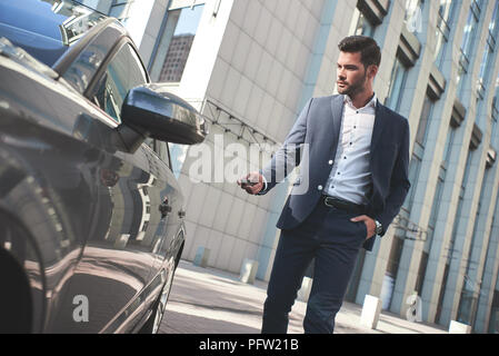 Questa vettura è perfetto per me. Allegro uomo maturo in convenzionale guardando la fotocamera e sorridere mentre in piedi vicino alla sua nuova vettura Foto Stock