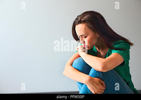 Ritratto di una donna triste guardando pensieroso circa i suoi problemi di fronte a un muro grigio Foto Stock