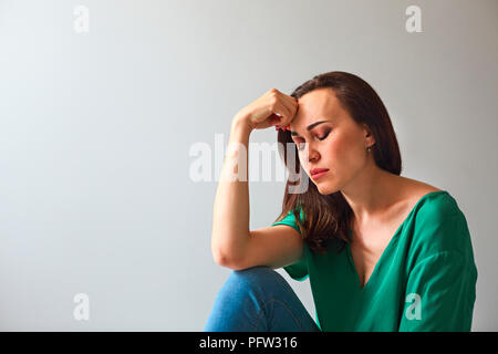 Ritratto di una donna triste guardando pensieroso circa i suoi problemi di fronte a un muro grigio Foto Stock