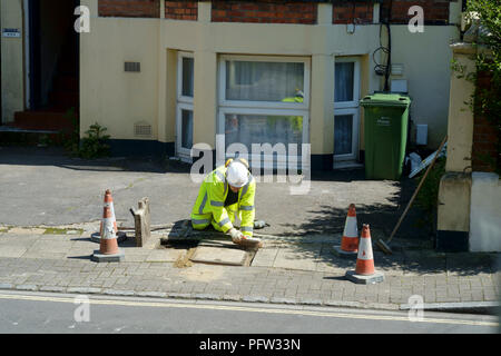 Workman indossando alta visibilità abbigliamento di sicurezza di eseguire delle riparazioni per un coperchio di scarico su un marciapiede a Southsea England Regno Unito Foto Stock