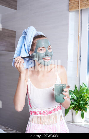 Donna di applicare la maschera idratante crema per la pelle sulla faccia guardando nello specchio del bagno. Ragazza prendersi cura della sua carnagione crema idratante di stratificazione. Dermocosmesi spa Foto Stock