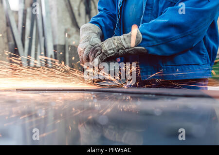 Lavoratore in metallo macinazione in fabbrica il pezzo con la formazione di scintille battenti Foto Stock