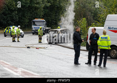 Fire il personale di servizio e gli ufficiali di polizia frequentare la scena di un incendio di un rosso auto Renault a Crumlin, South Wales, Regno Unito Foto Stock