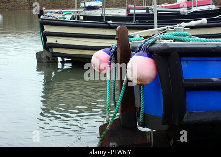 Rosa chiaro e blu parafanghi boe o proteggere la parte posteriore di una piccola barca in un porto Foto Stock