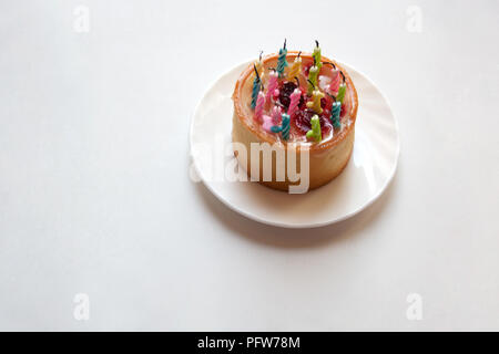 Piccola torta di compleanno con candele luminose su sfondo bianco con spazio di copia Foto Stock