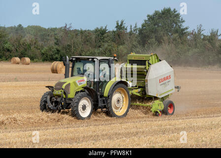 Claas il trattore e la rotopressa rendendo le balle di paglia in un campo. Foto Stock