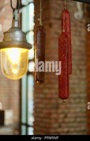 Sausagees affumicato appeso ad un gancio sotto il soffitto. Foto con profondità di campo ridotta. Foto Stock