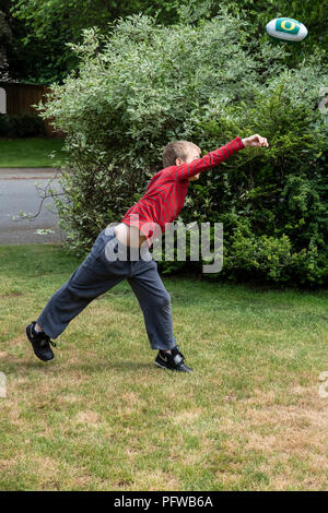 10 anno vecchio ragazzo gettare un calcio sul suo prato Foto Stock