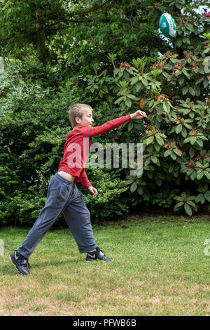 10 anno vecchio ragazzo gettare un calcio sul suo prato Foto Stock