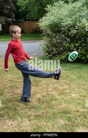 10 anno vecchio ragazzo calci un calcio sul suo prato Foto Stock