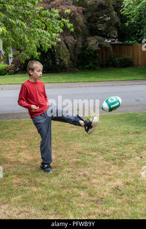 10 anno vecchio ragazzo calci un calcio sul suo prato Foto Stock