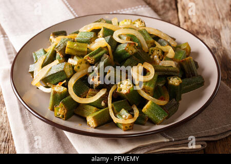 Cucina vegana: speziate okra soffritto con cipolla close-up su una piastra sul tavolo orizzontale. Foto Stock