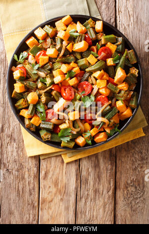 Ricetta tradizionale ragù da okra, patata dolce, pomodori, cipolle ed erbe close-up su una piastra su un tavolo. Verticale in alto vista da sopra Foto Stock