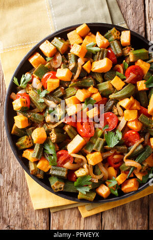 Salute organico cibo cotto okra, patate dolci, pomodori, cipolle ed erbe closeup su una piastra sul tavolo. Verticale in alto vista da sopra Foto Stock