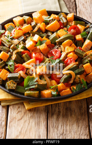 Cibo vegetariano: stufato okra, patate dolci, pomodori, cipolle ed erbe closeup su una piastra sul piano verticale. Foto Stock