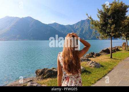 Vista posteriore del giovane donna con abito guardando il bellissimo paesaggio del lago di fronte a lei. Copia dello spazio. Foto Stock