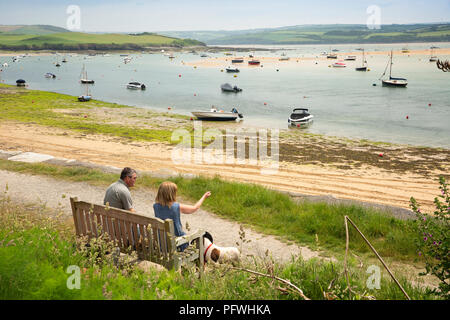 Regno Unito, Cornwall, Rock, giovane seduto sul banco di waterfront accanto al fiume Camel Foto Stock