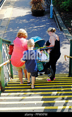 Una famiglia mano portando un bimbo nel passeggino sulla passerella passeggeri alla stazione ferroviaria di Acle, Norfolk, Inghilterra, Regno Unito, Europa. Foto Stock