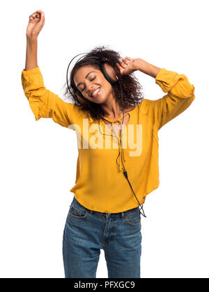 Attraente afro-americano di giovani donna l'ascolto di musica con cuffie e ballando sul muro bianco sullo sfondo. Ragazza in Giallo autunno top. Studio shot. Foto Stock