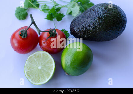 Avocado, lime tagliato a metà, pomodori sulla vite e coriandolo/koriander collocato in un gruppo su sfondo bianco Foto Stock