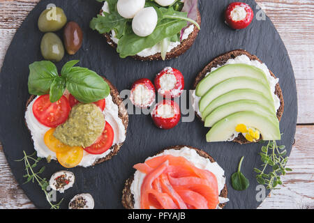 Crostino con salmone, avocado, mozzarella, pomodoro, pesto,olive, crema di formaggio. Mix di diversi spuntini e stuzzichini Foto Stock