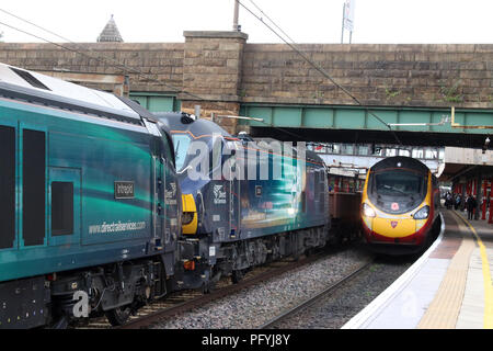Il Pendolino elettrico treno arrivando alla stazione di Lancaster su WCML passando DRS treno merci con la classe 66 e Classe 88 locomotive fermo sulla linea veloce. Foto Stock
