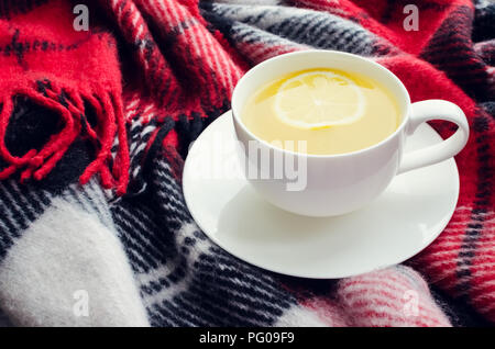 Tazza di tè con limone sul rosso calda coperta di lana. Bevanda calda per i freddi giorni di pioggia. Hygge danese concetto, autunno dell'umore. Accogliente inverno mattina a casa. Caldo Foto Stock