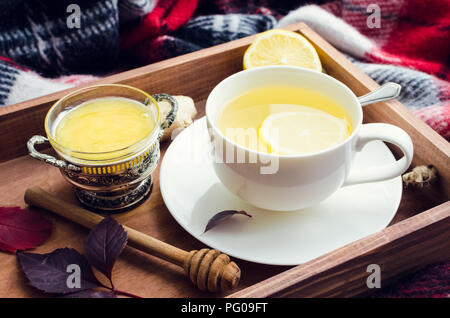 Salutare tè allo zenzero con miele, radice di zenzero e limone sul vassoio in legno con autunno caduta foglie sul rosso calda coperta di lana. Bevanda calda per il freddo giorno di pioggia Foto Stock