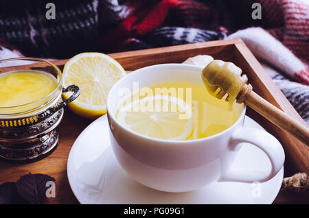 Salutare tè allo zenzero con miele, radice di zenzero e limone sul vassoio in legno con autunno caduta foglie sul rosso calda coperta di lana. Bevanda calda per il freddo giorno di pioggia Foto Stock