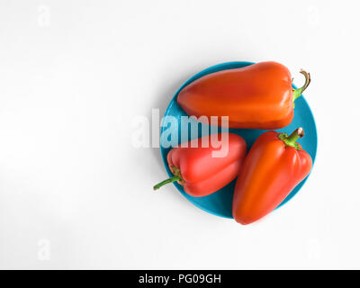 Peperone rosso in vista dall'alto modello di foto con spazio copia piastra blu con tre peperoni rossi dolci è in piedi su un tavolo bianco Foto Stock
