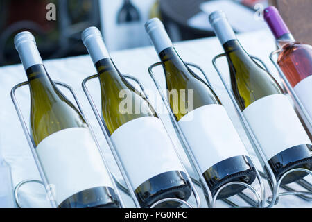 Bottiglie di vetro con vino bianco in fila sul tavolo in piedi in rack in metallo. Bellissimo concetto bevanda decorazione. Close up, il fuoco selettivo Foto Stock