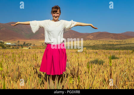 Giovane donna con le braccia aperte e guardando la telecamera in aloe vera in campo Fuerteventura, Isole Canarie, Spagna. Foto Stock