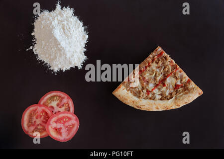 Fetta di tonno al forno pizza, mucchio di farina e fette di pomodoro su sfondo nero Foto Stock