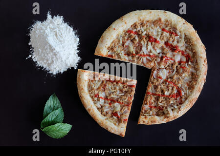 Tonno al forno pizza, mucchio di farina e foglie verdi su sfondo nero Foto Stock