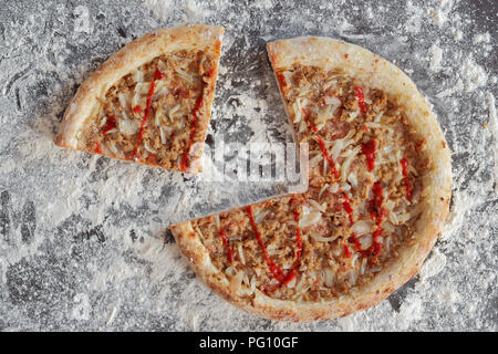 Fette di pizza al tonno su sfondo scuro con sparsi di farina bianca Foto Stock