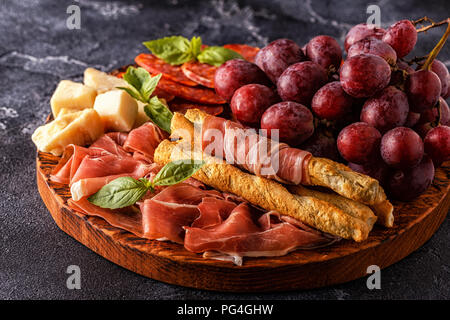 Il prosciutto, salsiccia vino, uva, parmigiano sul tavolo scuro, il fuoco selettivo. Foto Stock