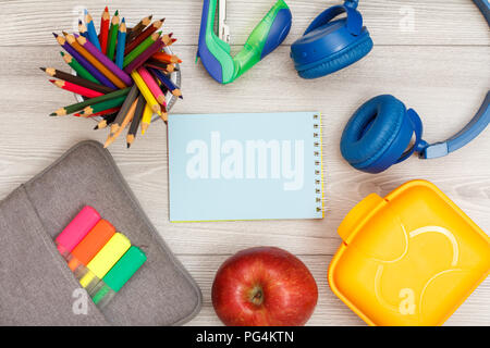 Sacchetto custodia a matita con colore pennarelli e marker matite di colore, Apple notebook blu, cucitrice, cuffie e scatola di pranzo in grigio sullo sfondo di legno. Parte superiore Foto Stock