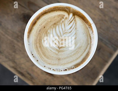 Cappuccino caffè in un bicchiere di carta, con un pattern di foglia sulla superficie della schiuma di latte Foto Stock