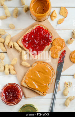 Yummy marmellata e burro di arachidi vasetti, tradizionale panino e cracker, top-vista. Carta da forno, sullo sfondo di legno. Classic dolci. Foto Stock