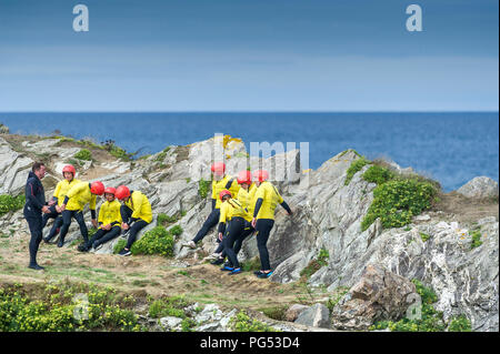 Un gruppo di turisti in ascolto di un istruttore dando un parlare di sicurezza prima di avviare una sessione di coasteering sul promontorio in Newquay, Cornwall. Foto Stock