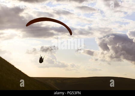 Un parapendio si stagliano contro il cielo sopra Edale Valle del Peak District, Derbyshire. I piloti di sollevamento di guadagno dalla forte corrente ascensionale che occu Foto Stock