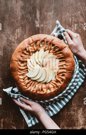 Ritagliato colpo di donna con biancheria tenendo in casa torta di mele sul tagliere di legno Foto Stock