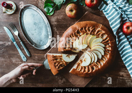 Vista parziale di donna con torta server tenendo pezzo di fatti in casa torta di Apple sul tagliere di legno Foto Stock