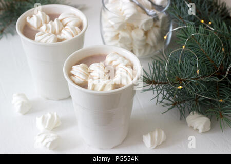 Il cacao con marshmelow in bianco tazze e marshmallows in un vasetto di vetro su un tavolo bianco con rami di abete rosso, una ghirlanda di fiori e una stella bianca. Messa a fuoco selettiva Foto Stock